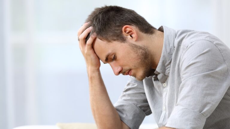 sad man holding head with hand sitting on sofa