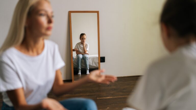 Reflection in mirror detached sad little girl during stressed mother scolding