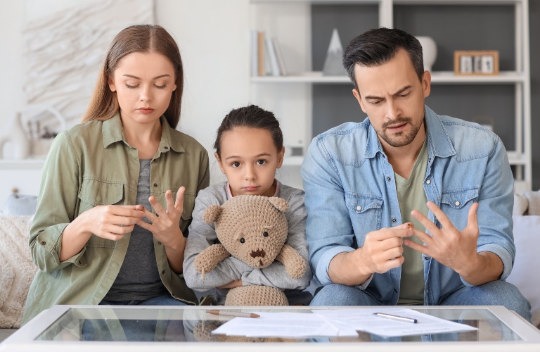 Sad little girl with toy and her parents taking off their wedding rings at home
